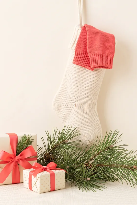A cream stocking with a coral cuff, pine sprigs and two small wrapped gifts.