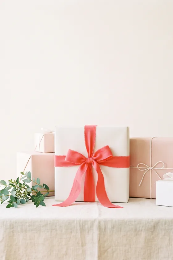 A gift table of blush and cream boxes, one tied with a wide coral bow.