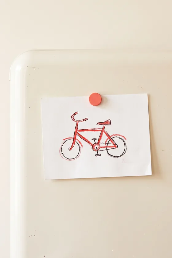 A child's crayon drawing of a red bicycle pinned to a fridge door.